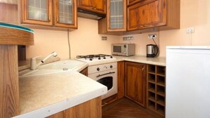 A compact kitchen with wooden cabinets, a gas stove, a microwave, and a refrigerator. - 1 Bedroom Apartment Knyazya Leva 2 (Lviv)