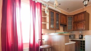 A kitchen with wooden cabinets, a bar stool, and a window with red curtains. - 1 Bedroom Apartment Knyazya Leva 2 (Lviv)