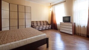 A bedroom with a bed, a sofa, a TV on a dresser, and a wardrobe. - 1 Bedroom Apartment Knyazya Leva 2 (Lviv)