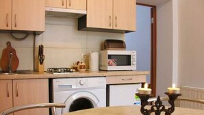 A compact kitchen with a microwave, toaster, and washing machine. There is a table with a candle holder.