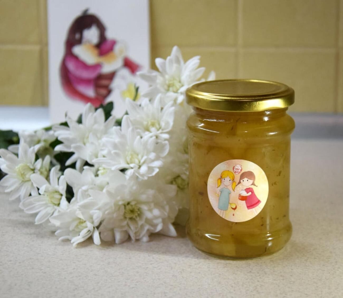 A jar of pickled vegetables with a gold lid, placed next to white flowers on a countertop.