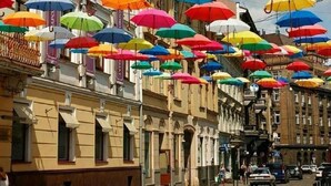 A street lined with buildings, some with colorful umbrellas hanging overhead.