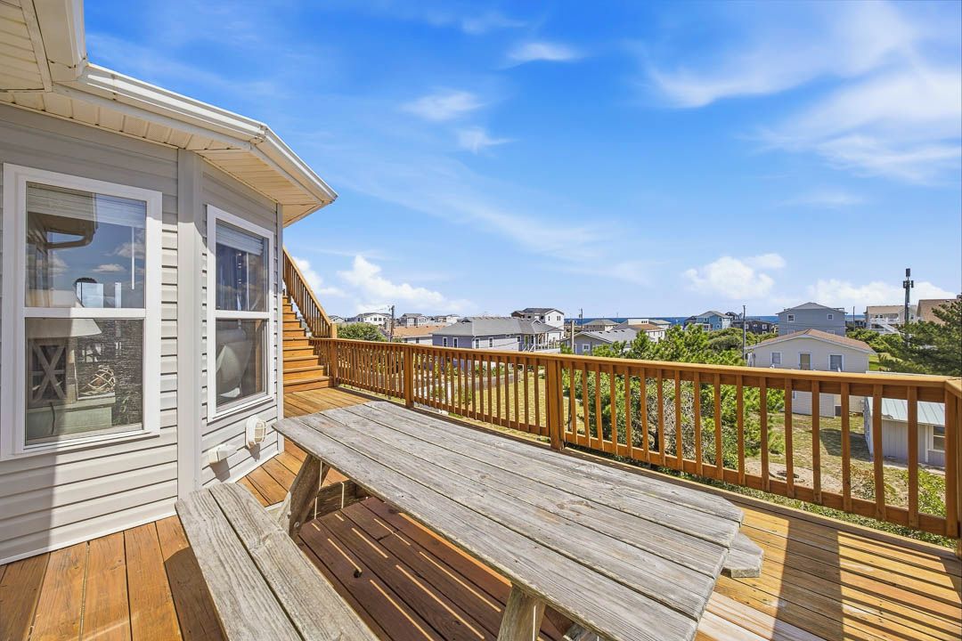 A wooden deck with a bench, a staircase leading to a covered area, and a view of neighboring houses.