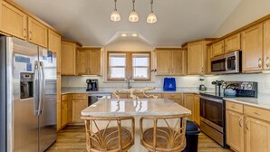 Una cocina con armarios de madera, un refrigerador de acero inoxidable, un microondas y una isla grande con sillas.