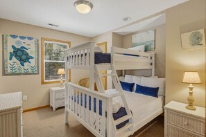 A room with bunk beds, a small bedside table with a lamp, and artwork on the walls.