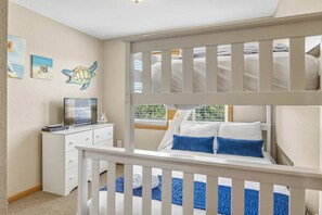 Une chambre d’enfant avec des lits superposés, une commode, un téléviseur et des décorations murales.