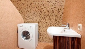 A compact bathroom with a washing machine, a sink, and a tiled backsplash.