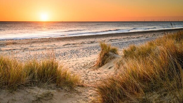A beach with sand and grass in the foreground, and the ocean in the background.