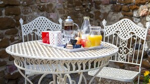 A round metal table with a tray of breakfast items including a coffee pot, mugs, and fruit.