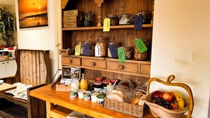 A wooden display shelf with jars labeled with tags, a wicker basket with fruits, and a table with various food items.