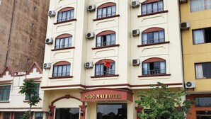 A multi-story hotel with a prominent entrance, air conditioning units, and a red car parked in front. - Ngoc Mai Hotel (Bai Chay)