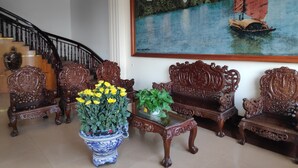 A grand staircase with ornate wooden railings, a large painting of a sailboat on water, and a potted plant with yellow flowers. - Ngoc Mai Hotel (Bai Chay)