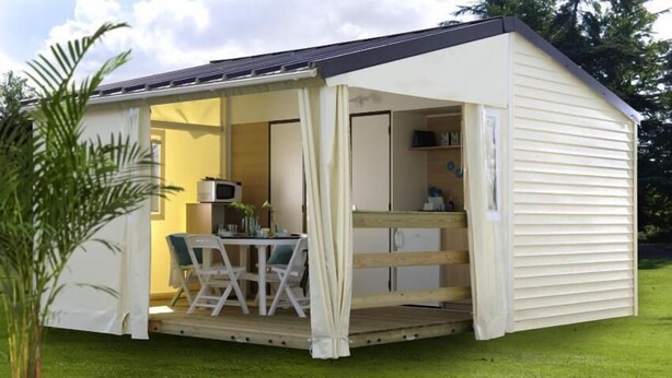 Een klein, laag gebouw met een overdekt terras, een tafel, stoelen en een zichtbare magnetron van binnen.
