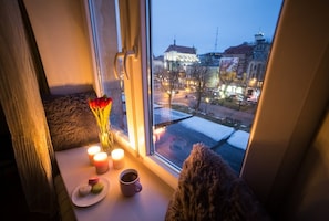 A window view of a cityscape at dusk with a table featuring candles, a vase with flowers, and a plate of pastries.