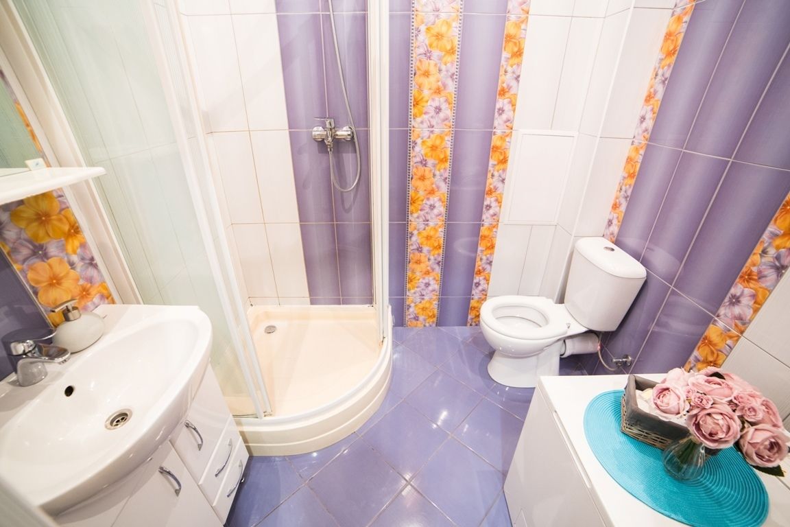 A bathroom with a shower, toilet, sink, and a decorative vase with flowers.