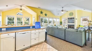 A kitchen with a large island, white cabinets, and a grey sofa in a living area. - Bama Breeze | Sound Side | Private Pool, Hot Tub | Kitty Hawk (Kitty Hawk)