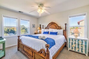 Ein Schlafzimmer mit einem hölzernen Bett, großen Fenstern, einem Deckenventilator und einem dekorativen Schrank.