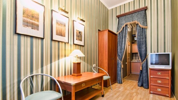 A room with striped wallpaper, a wooden desk with a lamp, a chair, a wardrobe, a television, and a mirror with curtains. - 1 Bedroom Apartment Ave. Svobody 31 (Lviv)