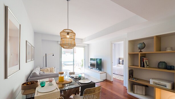 A modern living room with a glass dining table, wicker chairs, a television, and a bookshelf. - Petit Luxe Oasi d'Egara (Terrassa)