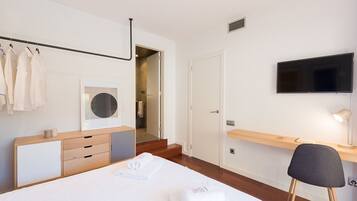 A modern hotel room with a bed, a desk, a chair, a TV, and a bathroom visible through an open door.