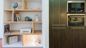 A modern kitchen with a built-in oven and microwave, wooden shelves with various items, and a globe on the top shelf. - Petit Luxe Oasi d'Egara (Terrassa)