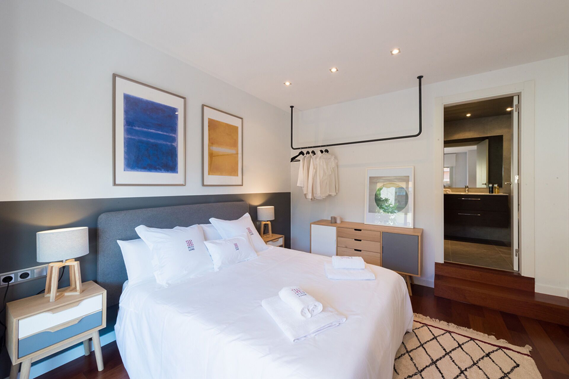 A modern hotel room with a large bed, bedside tables, a wardrobe, and a bathroom visible through an open door.