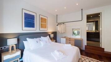 A modern hotel room with a large bed, bedside tables, a wardrobe, and a bathroom visible through an open door.