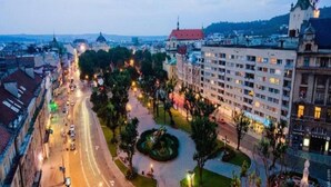 A cityscape with a prominent building featuring a red roof and a large, well-lit entrance. - 1 Bedroom Apartment Valova 16A (Lviv)
