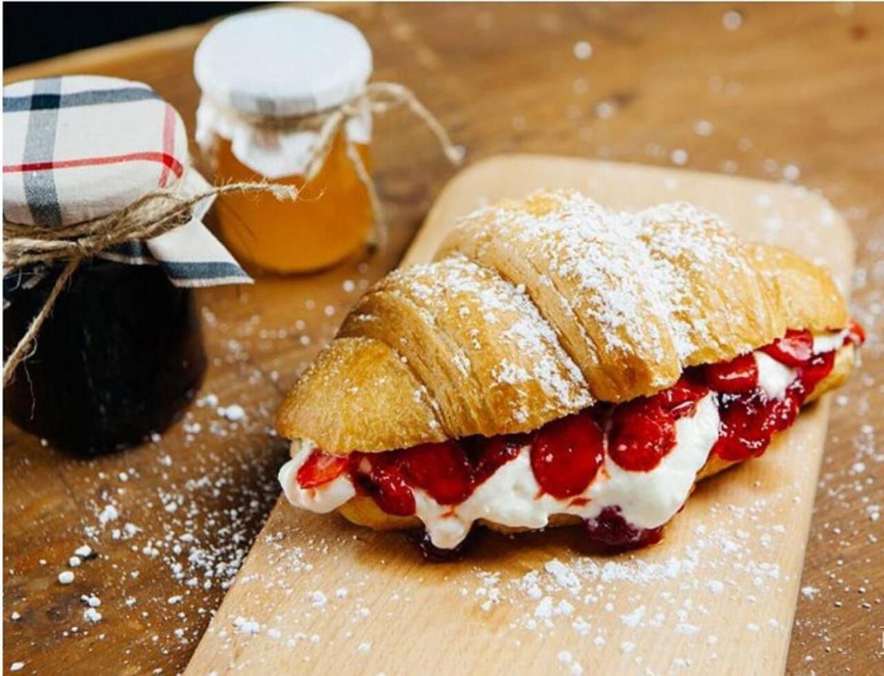 A pastry with whipped cream and red fruit filling, dusted with powdered sugar, on a wooden board.