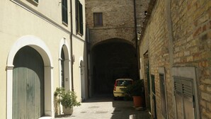 Un callejón estrecho con un arco de piedra, un coche aparcado y edificios con puertas y contraventanas arqueadas.