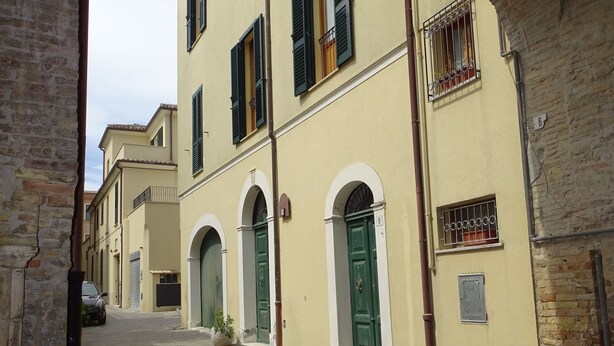 Una calle estrecha con edificios que tienen arcos y contraventanas verdes.