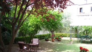 Un patio con una mesa y sillas, rodeado de plantas en macetas y árboles.
