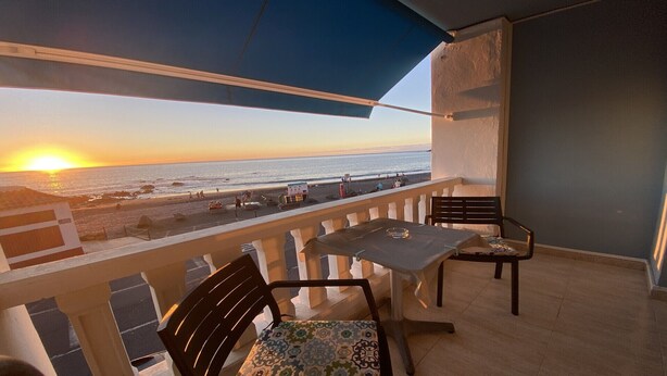 A balcony with a table and chairs, overlooking a beach at sunset. - Molino azul 1A (Valle Gran Rey)