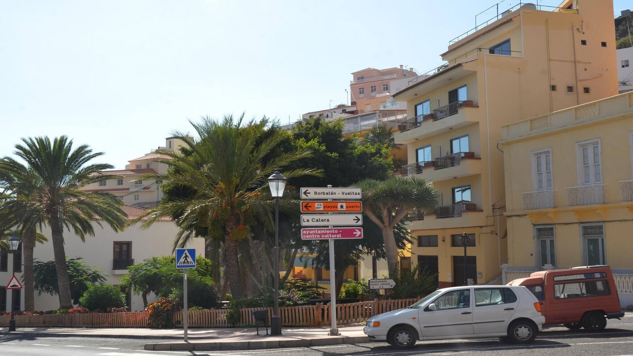 A street view with a directional signpost, a pedestrian crossing sign, and a parked car.
