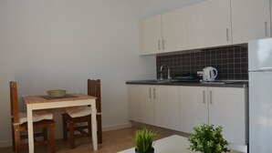 Cocina compacta con armarios de color claro, salpicadero de azulejos negros, hervidor blanco y una pequeña planta en maceta.