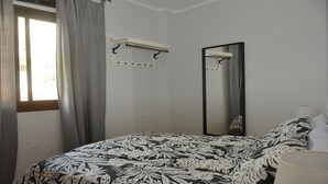 Un dormitorio con cama, ventana con cortinas, espejo y perchero.