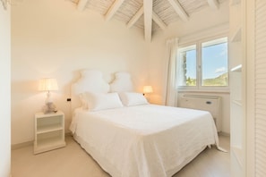 A bedroom with a large bed, two bedside tables with lamps, a window with curtains, and a view of the outdoors.