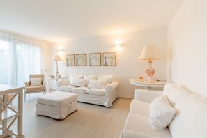 A white-themed living room with a sofa, ottoman, and two side tables with lamps.