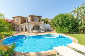 A swimming pool with lounge chairs, a stone building, and lush greenery.