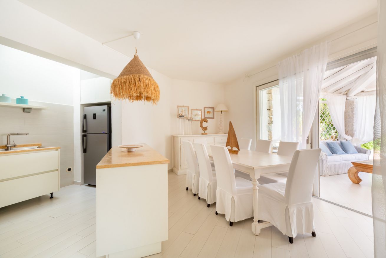 A modern kitchen with white cabinetry, a central island, and a dining area with white chairs.
