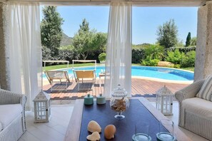 Zona de piscina amb una taula preparada per a dues persones, un recipient de vidre amb aperitius i vistes a una piscina i vegetació.