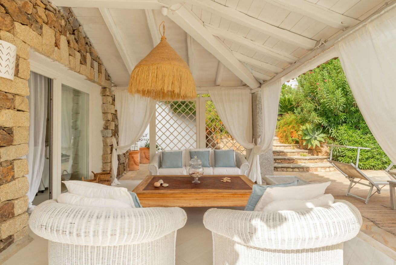 A covered outdoor seating area with wicker furniture, a wooden coffee table, and a hanging light fixture.