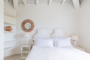 A white bedroom with a bed, a round mirror, and two bedside tables with lamps.