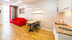 A modern kitchen with wooden countertops, a built-in oven, and a sink. There is a dining area with a wooden table and chairs, and a red sofa in the living area. - Apartment Mitskevicha 5a (Lviv)