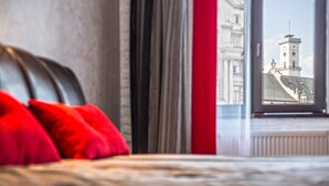 A bed with red pillows and a view of a building through a window. - Apartment Mitskevicha 5a (Lviv)