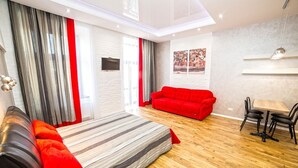 A modern room with a bed, a red sofa, a dining table with chairs, and a large window with curtains. - Apartment Mitskevicha 5a (Lviv)