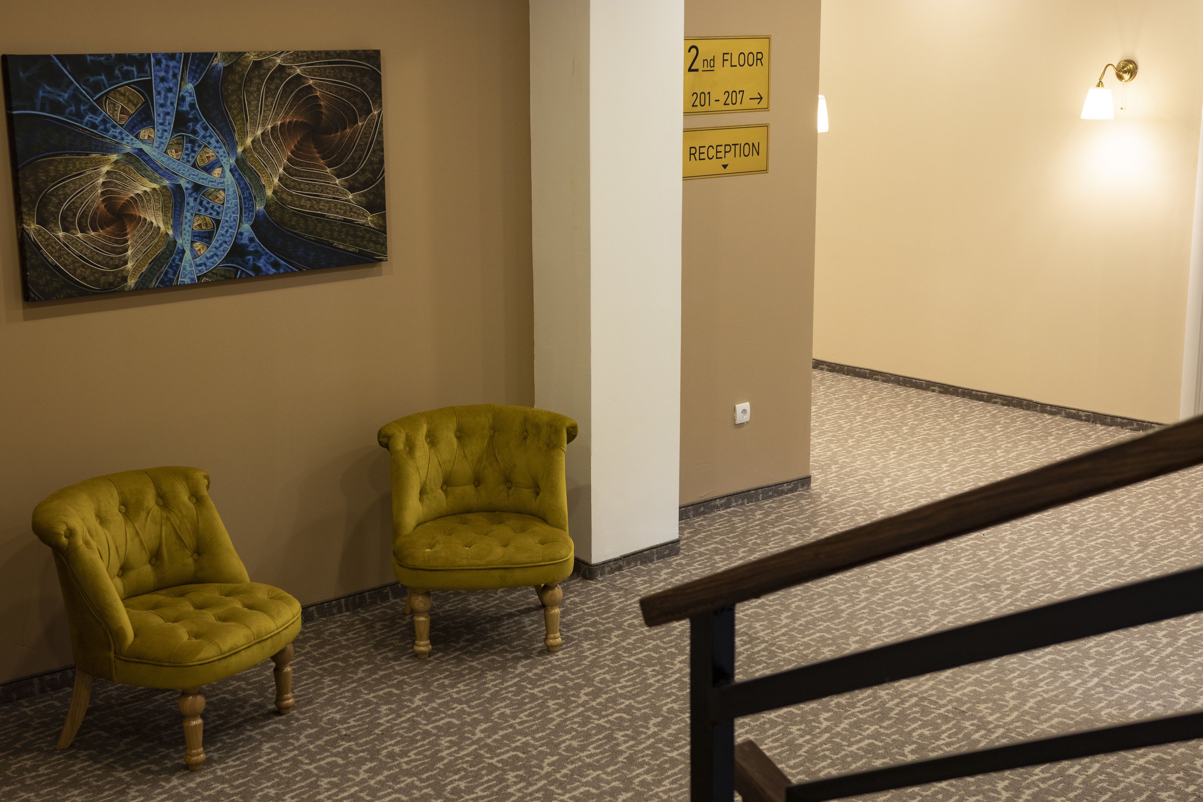 A hallway with two armchairs, a reception sign, and a wall with a blue abstract painting.