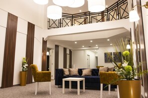 Un intérieur moderne avec un canapé bleu foncé, deux fauteuils dorés, une table basse blanche et une grande plante en pot.