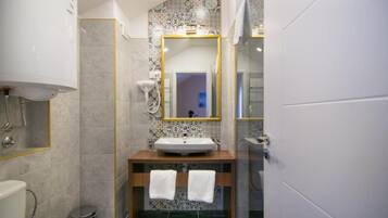 Un baño con un lavamanos blanco, un espejo con marco dorado y una zona de ducha.