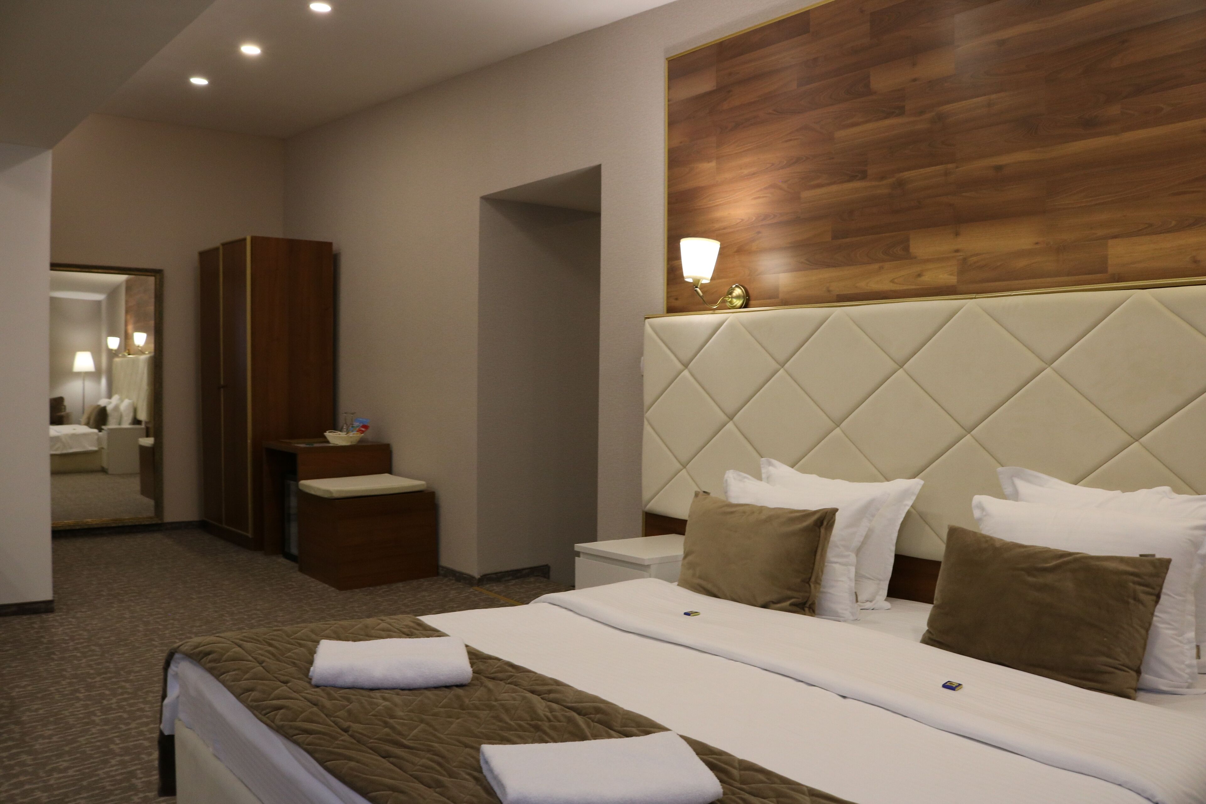 A hotel room with a large bed, a wooden headboard, a bedside table, a mirror, and a wardrobe.